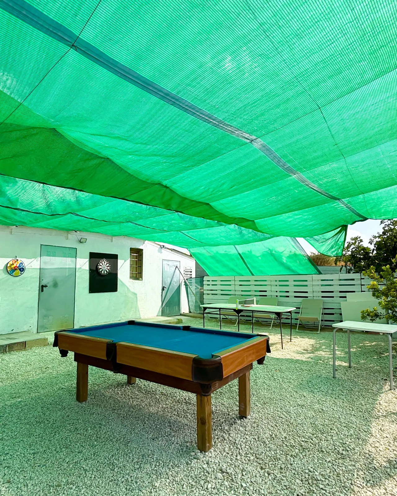 Mesa de billar y dardos bajo malla de sombra verde